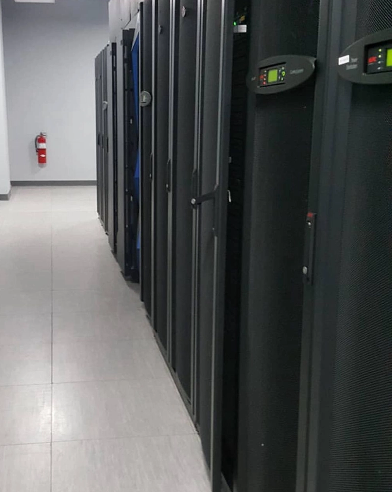 Pasillo de la sala de cómputo con la fila de gabinetes y las pantallas de distribución eléctrica en verde